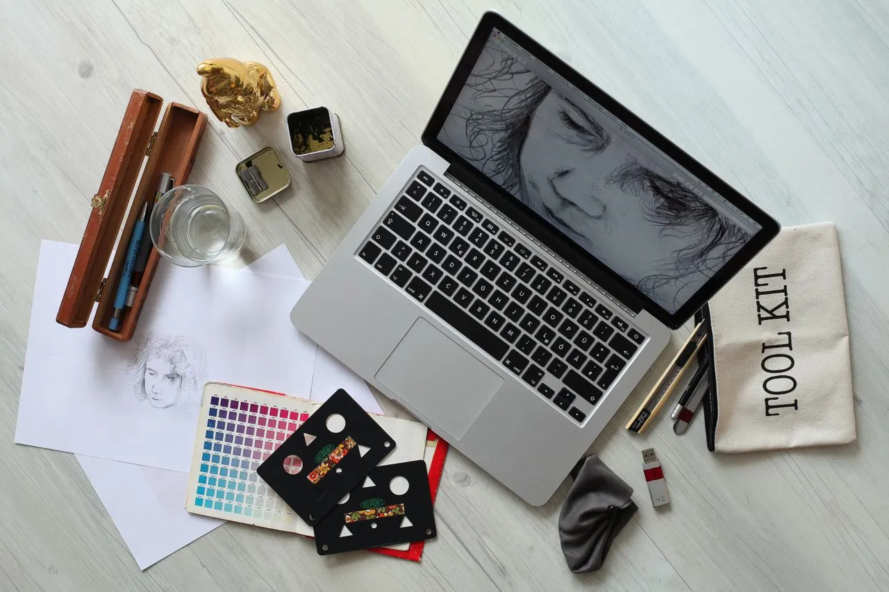 Escritorio de diseño con laptop, paleta de colores, bocetos y herramientas de dibujo