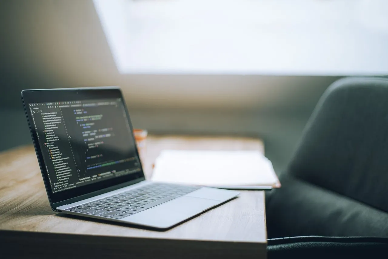 Laptop abierta mostrando código sobre un escritorio junto a una ventana