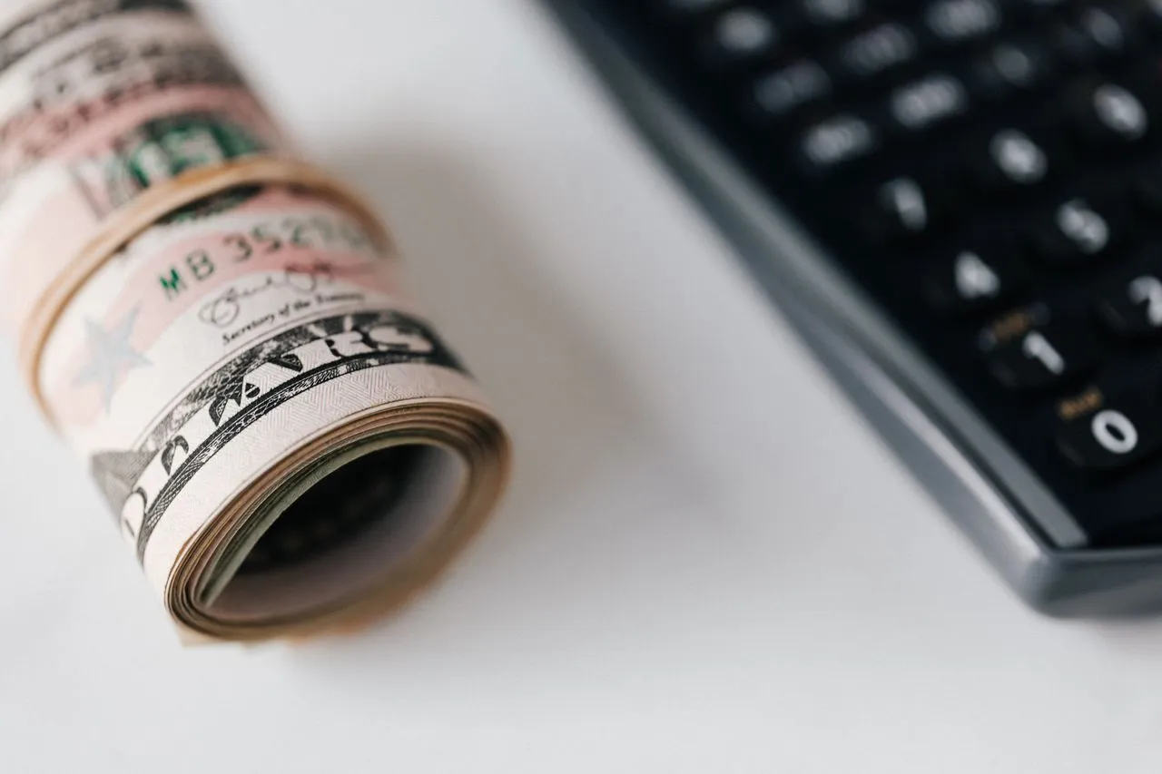Rollo de billetes de dólar junto a una calculadora sobre fondo blanco