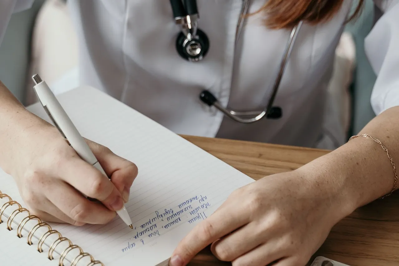 Manos de una médica escribiendo en un cuaderno con estetoscopio
