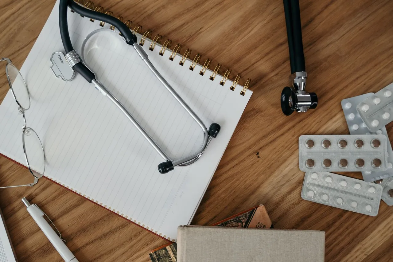 Cuaderno, estetoscopio, gafas y blísteres de medicamentos sobre una mesa de madera