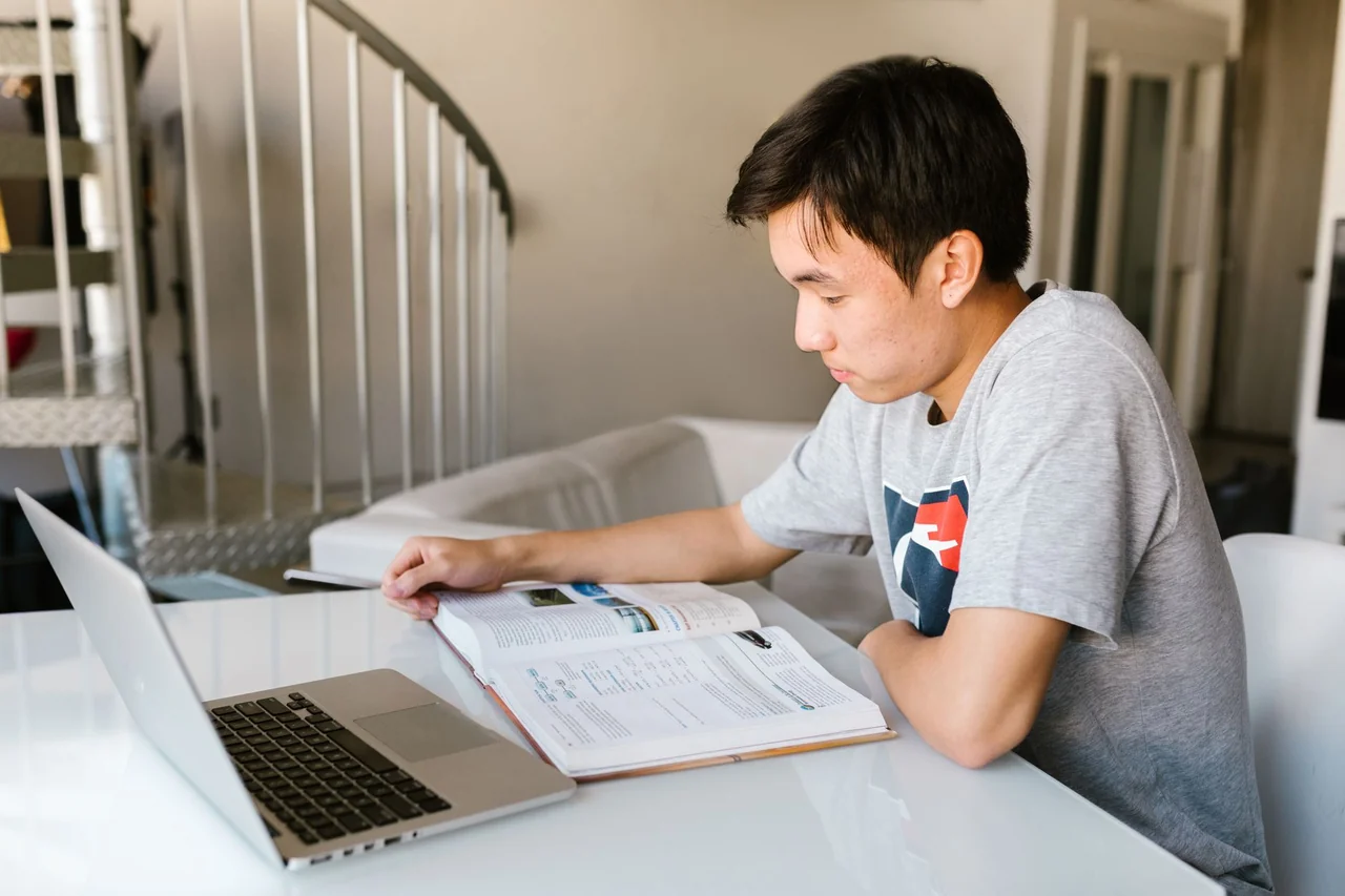 Estudiante estudiando en línea con laptop y libro